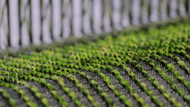 Green artificial turf being woven in factory