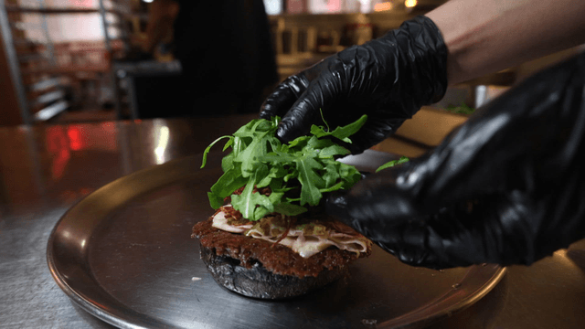 Arugula placed onto black burger bun on plate