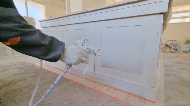 Worker painting wooden furniture with a spray gun