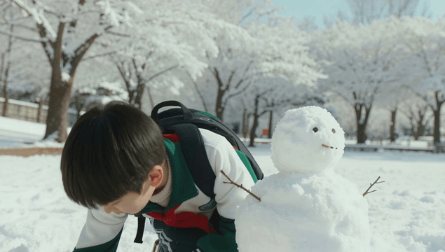 Happy boy building a snowman in a snow-covered park