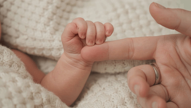 Newborn baby holding an adult's finger
