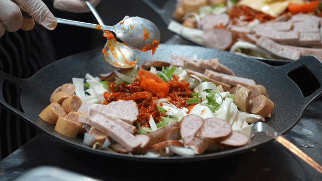 Chef adding seasoning with spoon to uncooked budaejjigae
