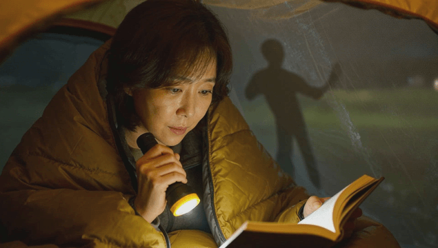 Woman reading book with flashlight inside tent