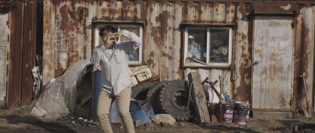 Man making a funny gesture in front of a rusty building