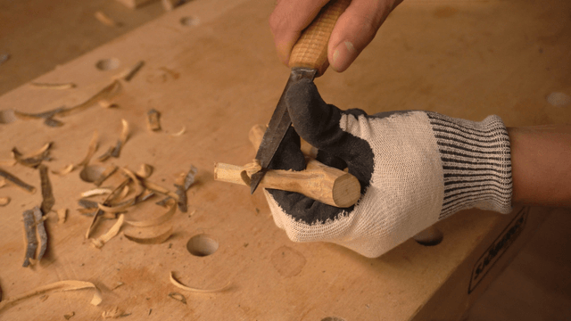 Hands carving wood with a knife on workbench