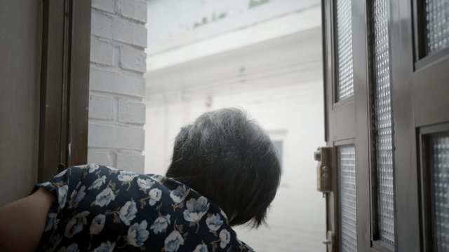 An elderly person looking out the door