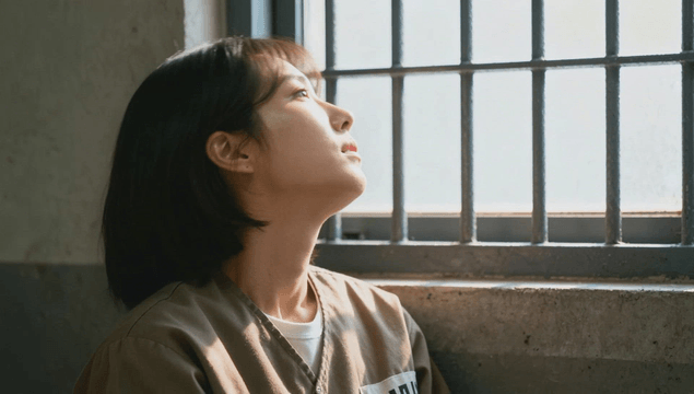 Female prisoner looking through bars toward window in cell
