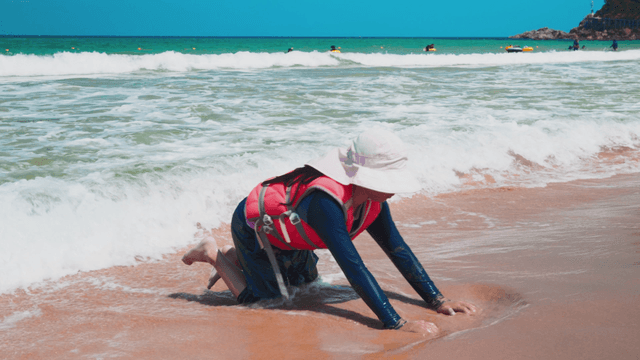 Girl digging sand while waves hit the beach
