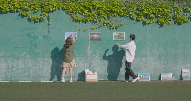 Two people arranging photos on a wall