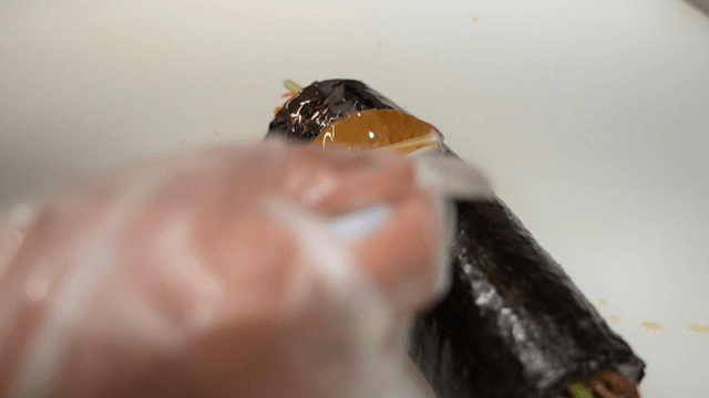Kimbap being brushed with sesame oil