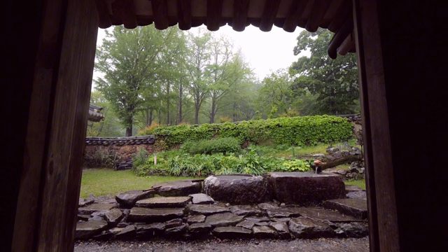 A view of the lush green landscape and rain from under the tiles