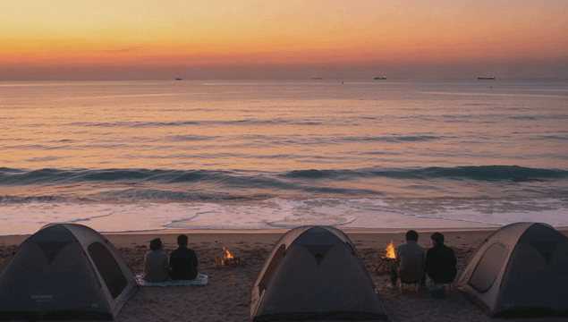 People camping by the beach with a bonfire at sunset