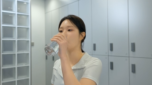 헬스장 라커룸에서 물을 마시는 젊은 여성