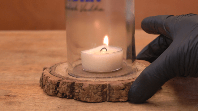 Candle on coaster being extinguished with a glass jar