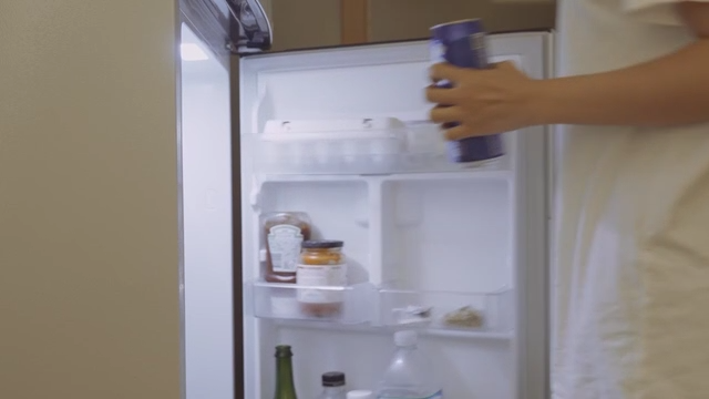 Young woman taking a can of beer out of the refrigerator