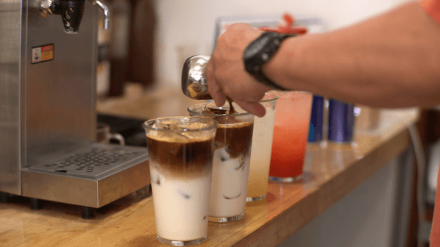 Barista pouring coffee into iced latte