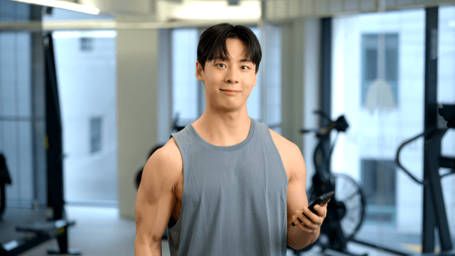 Young man lifting dumbbells while looking at smartphone
