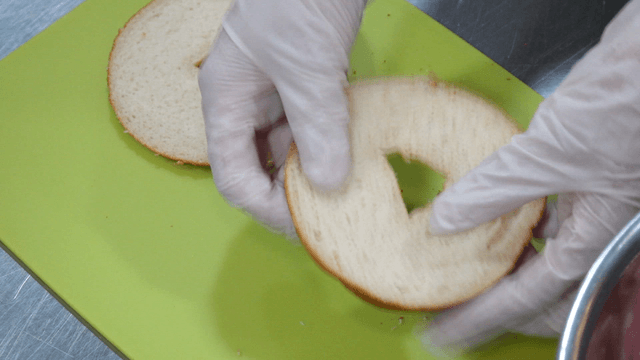 Preparing a bagel with gloved hands