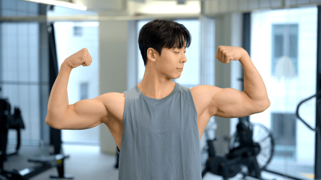 Young man flexing both arms at the gym