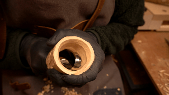 Artisan carving a hole in wooden piece with chisel