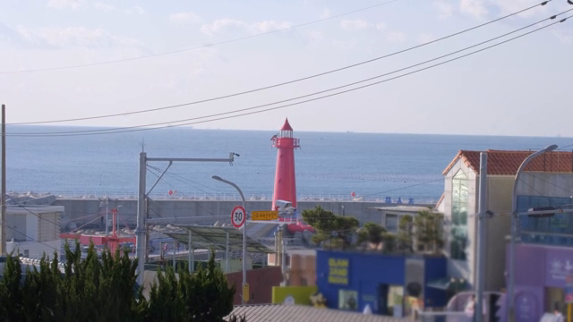Red lighthouse by the sea with buildings