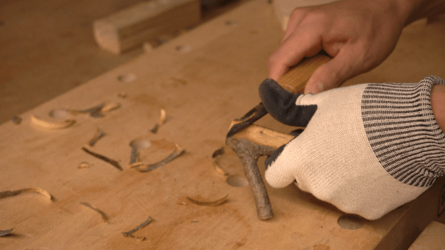 Hands carving a wooden branch with a knife