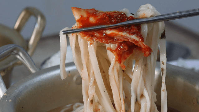 Chopsticks holding kimchi and chicken noodle soup
