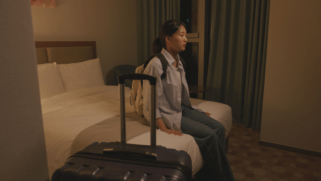Woman arrives and sits down on a hotel bed
