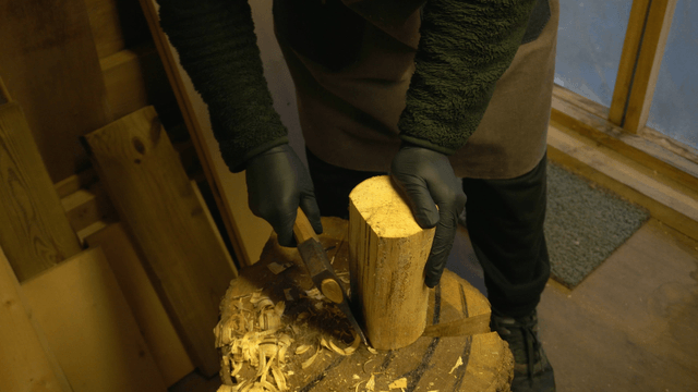 Carpenter shaping wood with an axe in workshop