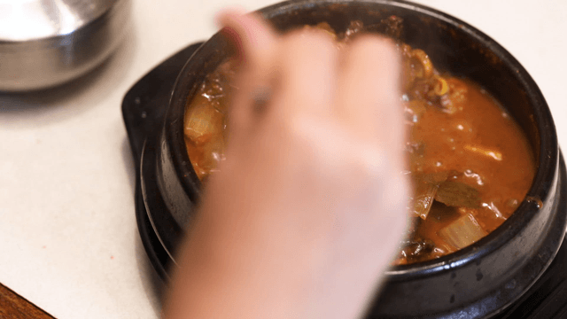 Stirring hot gatgimchi stew in earthen pot