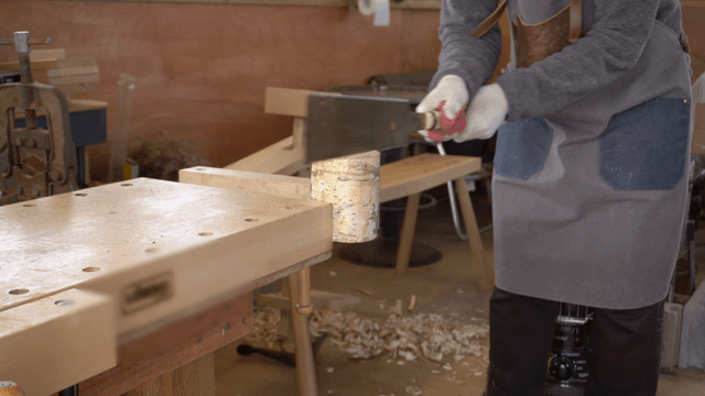 Carpenter cutting a log with a saw in workshop