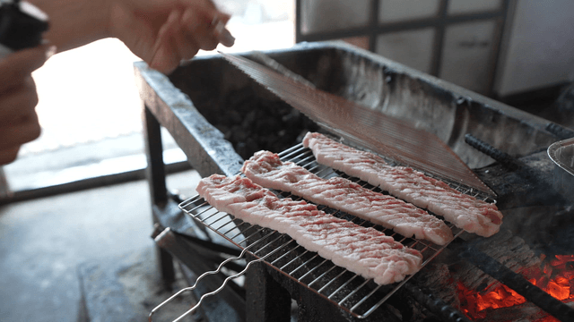 Salt being sprinkled over pork belly on charcoal fire