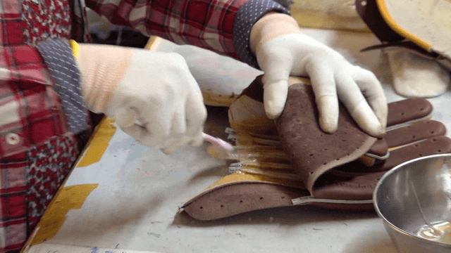 Worker applying glue to leather gloves on workbench