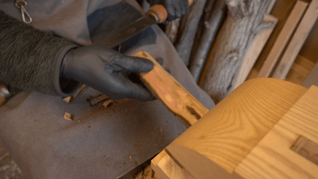 Artisan stripping bark from wooden branch with drawknife