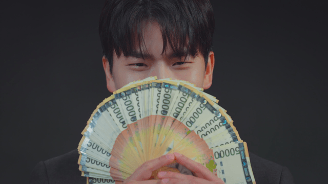 Man smiling with his mouth covered by money