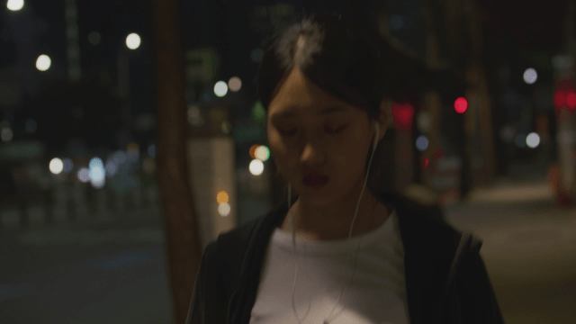 Young woman walking at night streer with earphones