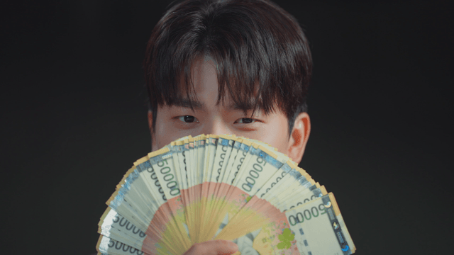 Man smiling with his mouth covered by money