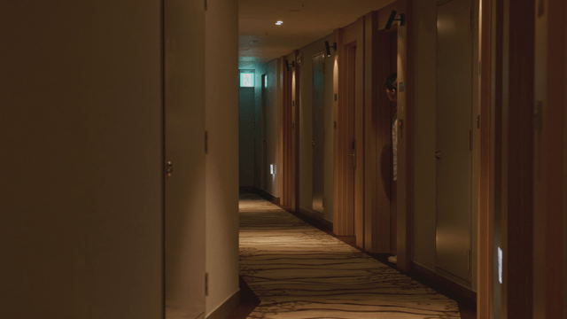 Woman peeking out from a hotel room hallway