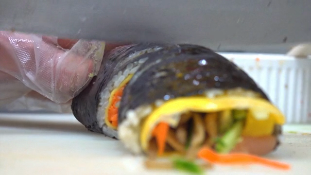 Kimbap being sliced on a cutting board