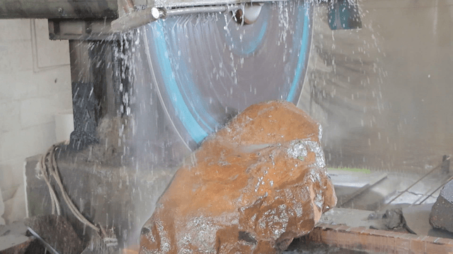 Industrial saw spraying water while cutting large stone