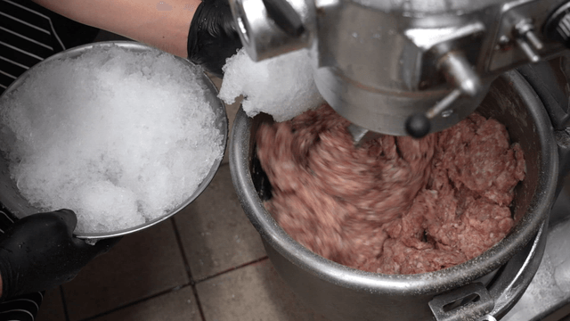 Chef mixing finely crushed ice with minced meat in industrial mixer