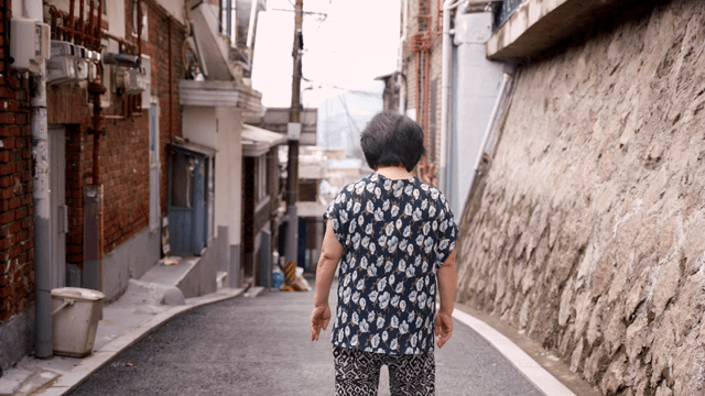 An elderly woman walking down a narrow alley