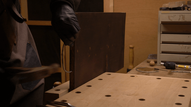 Artisan hammering metal wire into wooden board