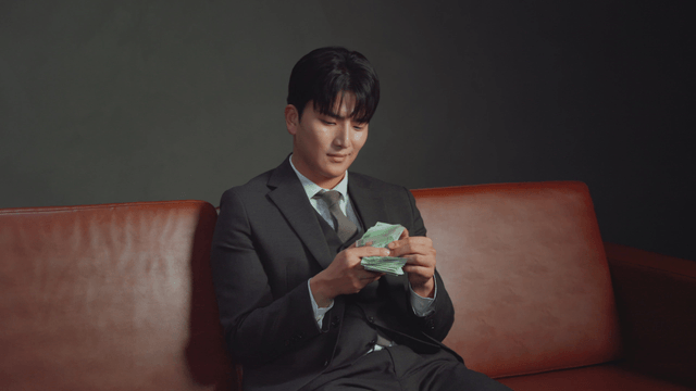 Man in a suit counting money on a sofa
