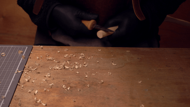 Hands carving wood on a workbench