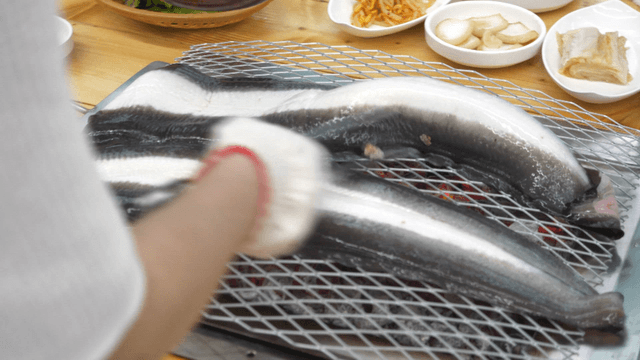 Large eel grilling over charcoal fire