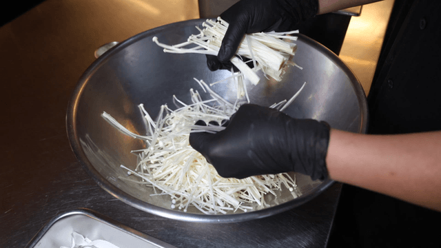 Chef tearing enoki mushrooms into bowl
