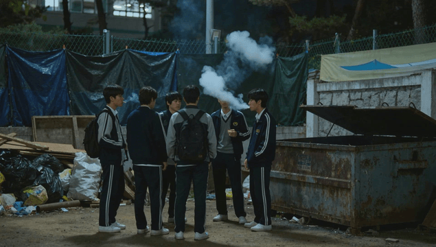 Male students smoking near trash bins at night