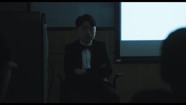 Male student in suit pointing after waking in dark classroom