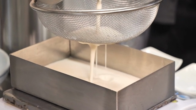 Soybean soup being strained into a metal container